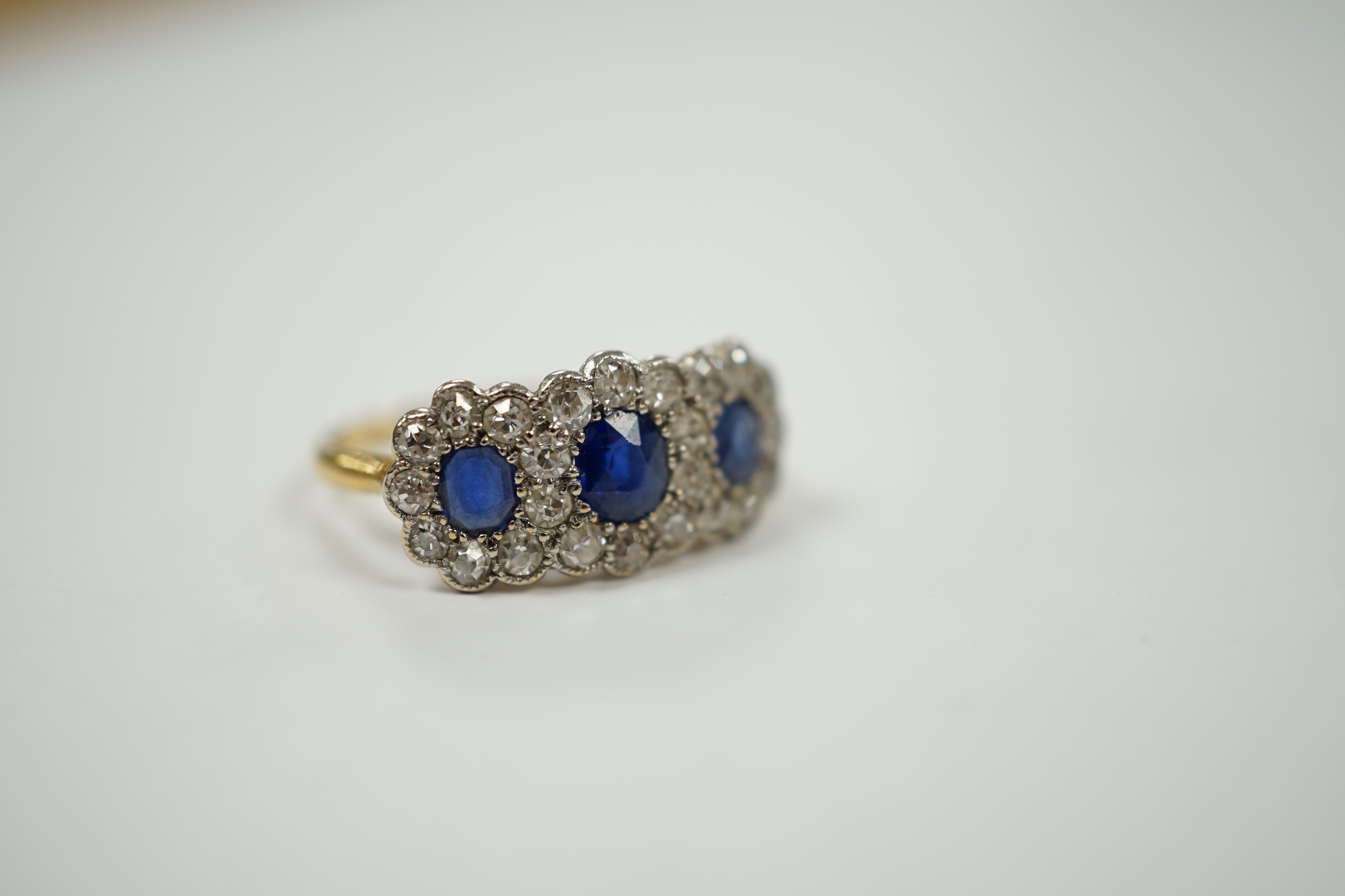 A yellow metal and millegrain set sapphire and diamond triple cluster ring, size K/L, gross weight 2.5 grams.